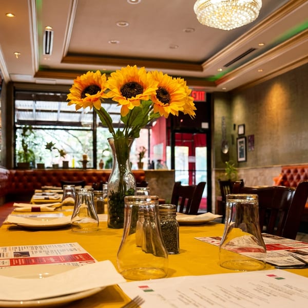 Restaurant dining room with red booths, yellow tablecloths, set tables, and a sunflower vase.