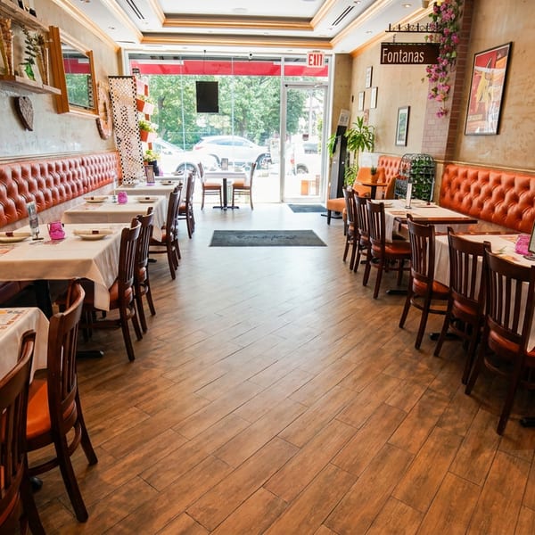 Fontanas restaurant interior with orange tufted booths, white-clothed tables, and wooden chairs.